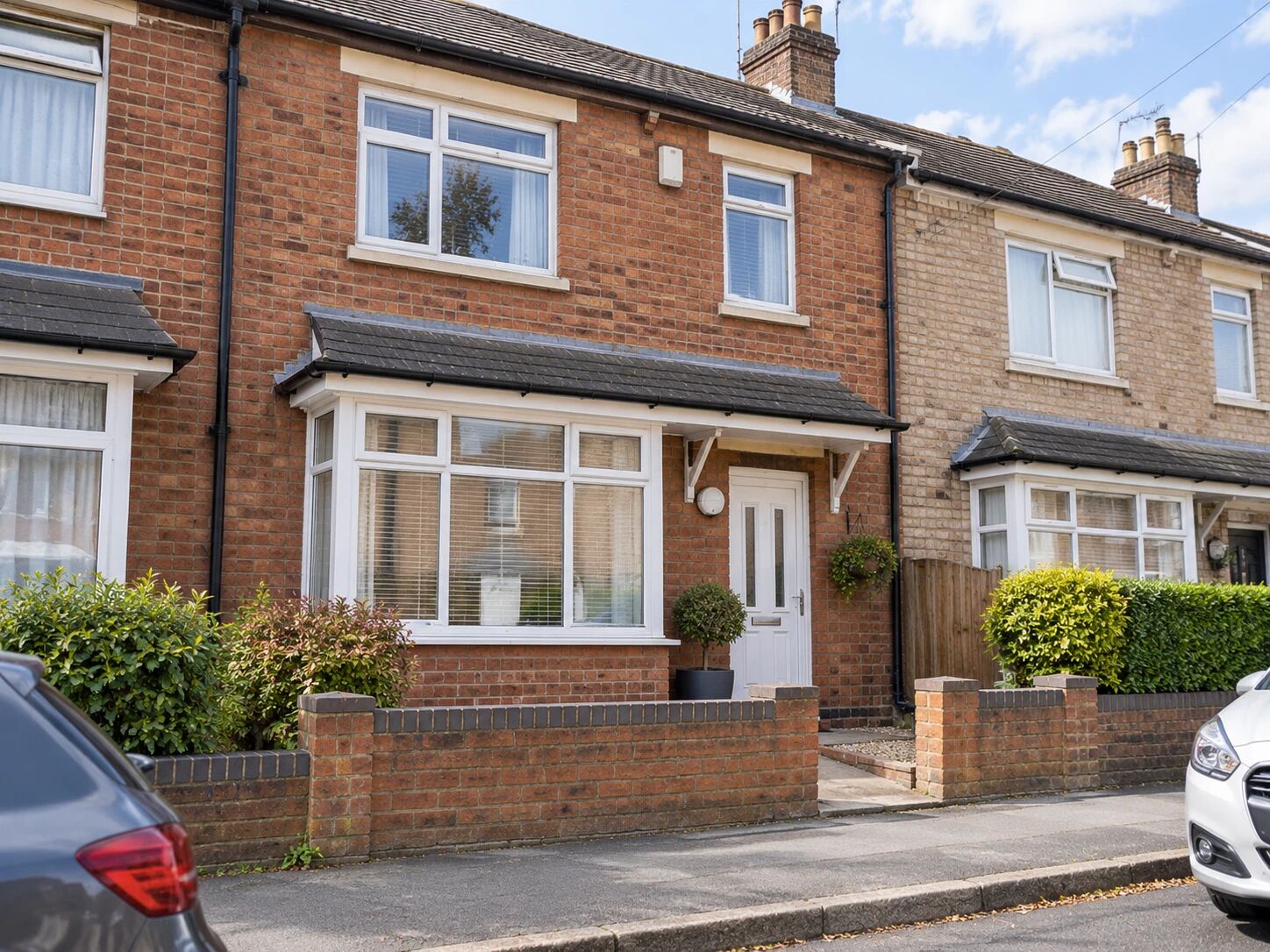 A well-kept red-brick terraced house with a white front door