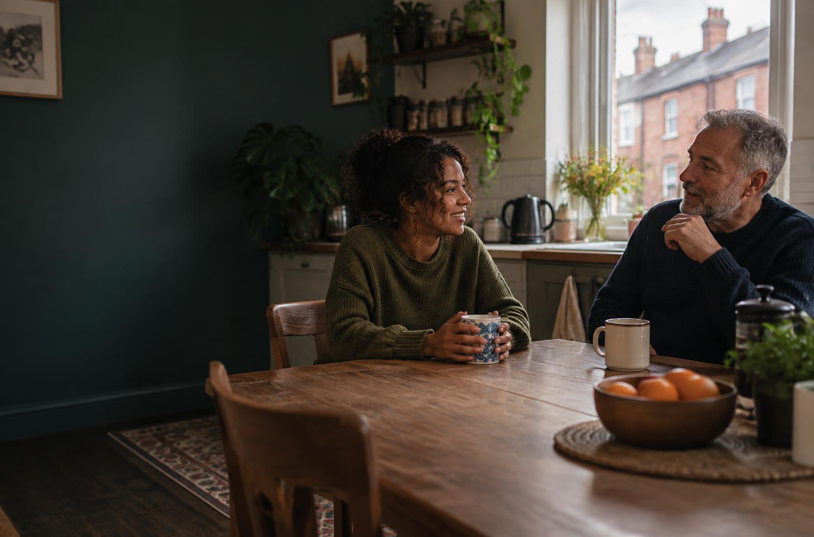 Two adults talking over tea at a kitchen table in a Bristol home